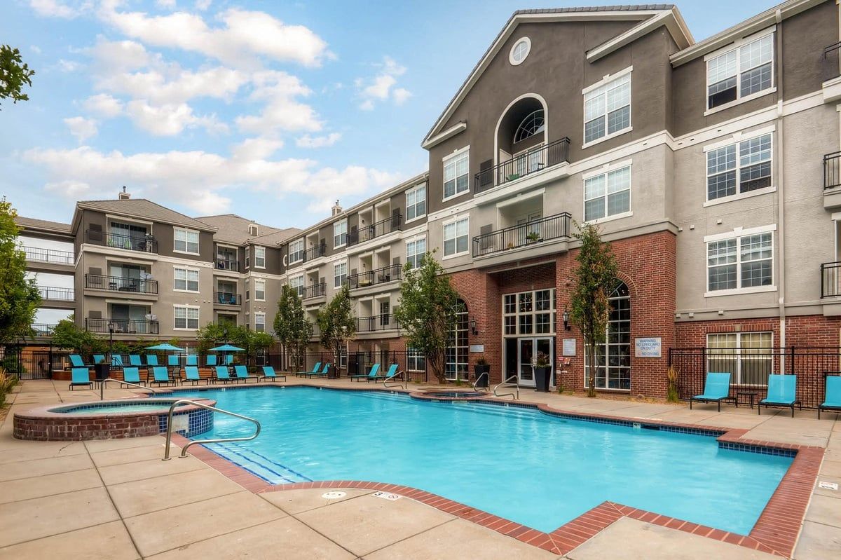 Apartment building with a pool. Blue water and lounge chairs in front of the multi-story building.