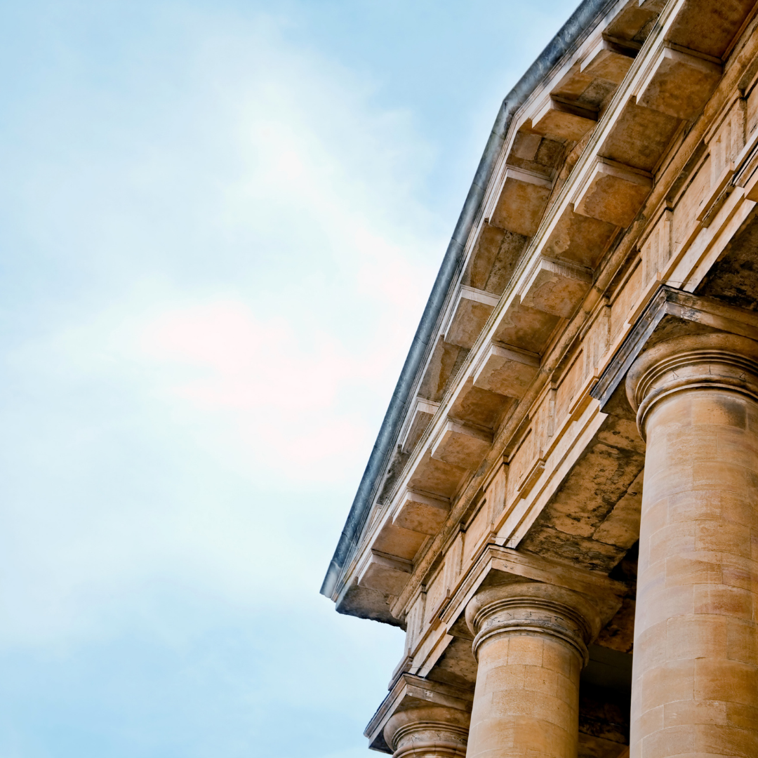 Looking up at the roof of a building with columns and a blue sky in the background.