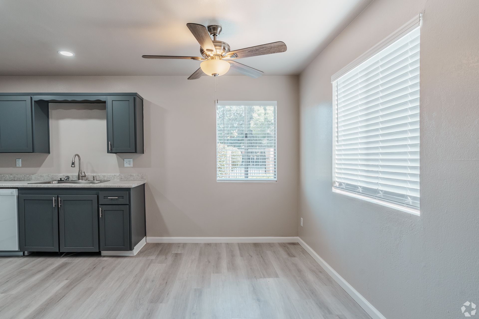 Gray kitchen with dark blue cabinets, ceiling fan, and windows with blinds.