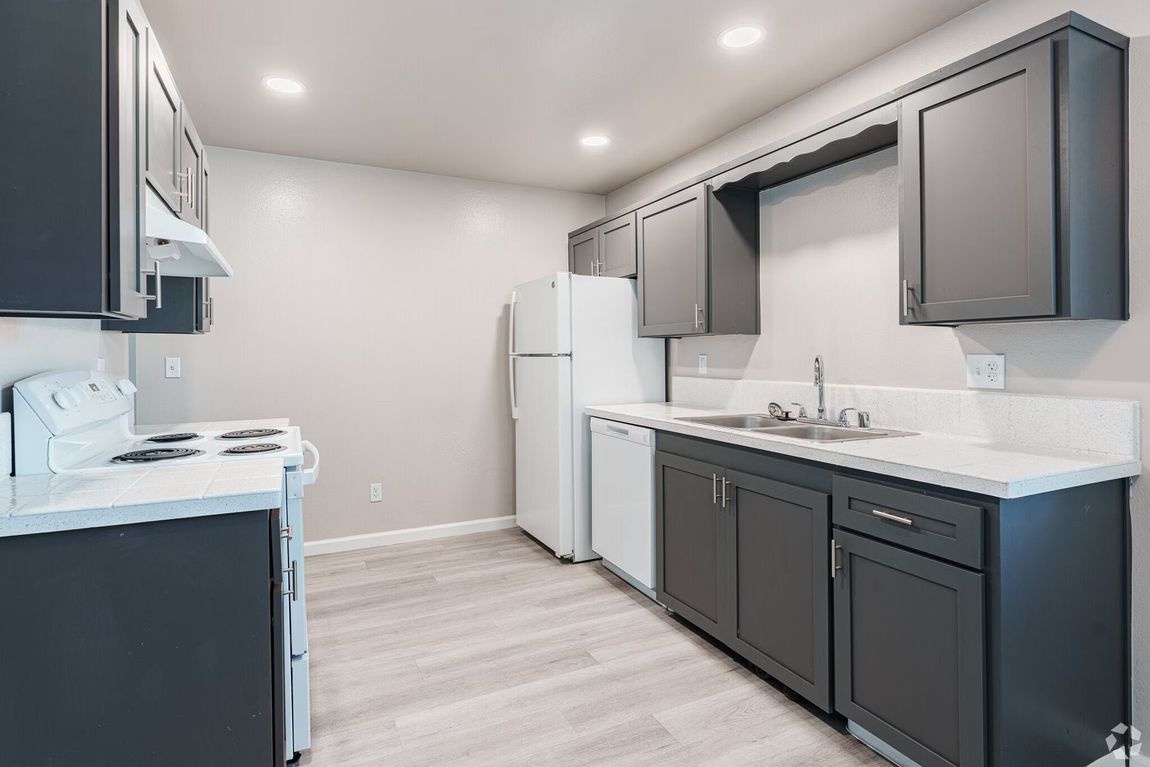 Dark gray kitchen cabinets, white appliances, light gray flooring, white countertops.