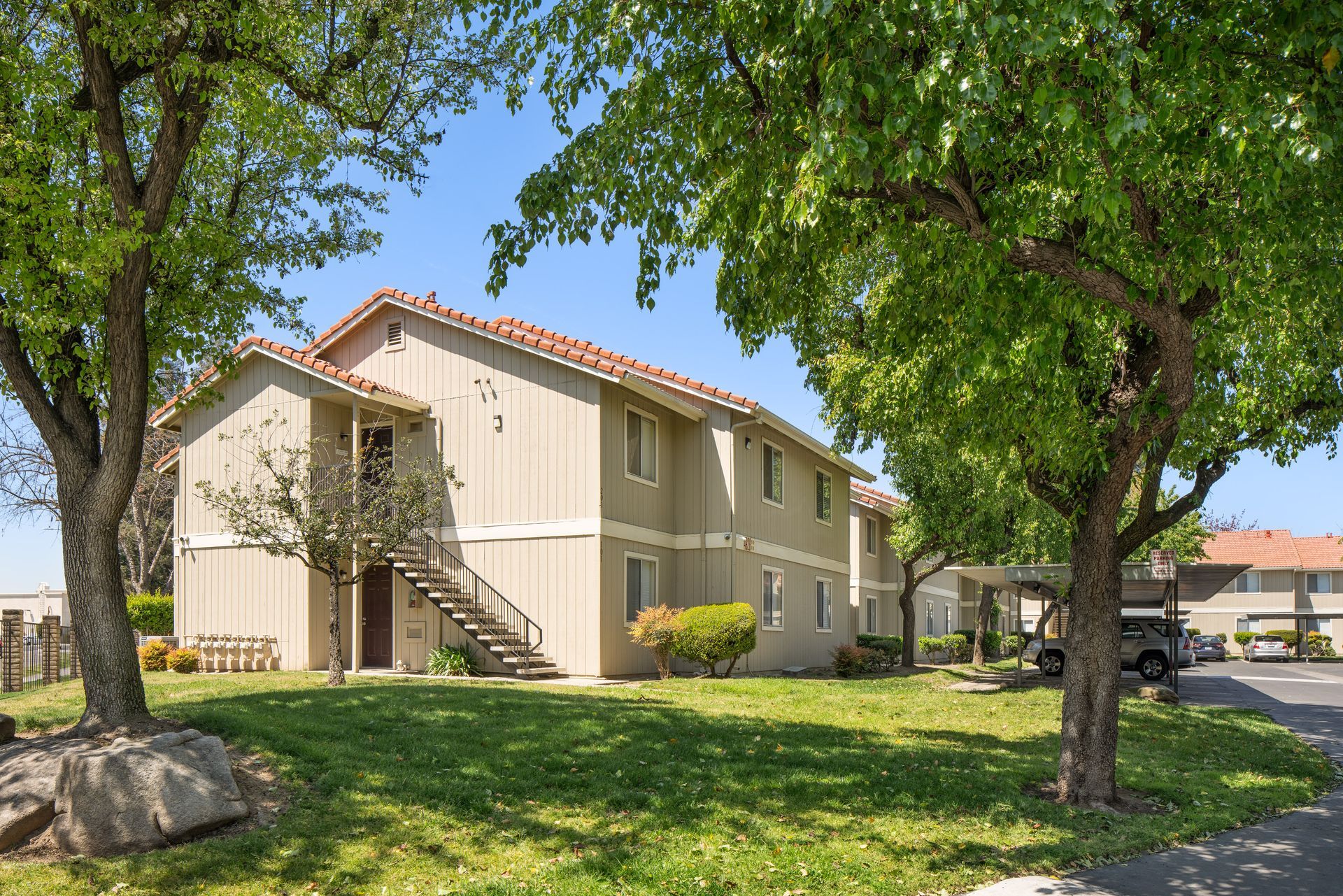 Apartment complex with green lawn, trees, and a blue sky with clouds.