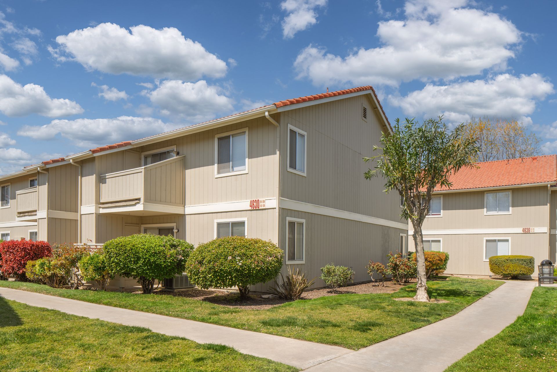 Apartment complex with beige walls, red tile roof, green grass, and a sunny, blue sky.