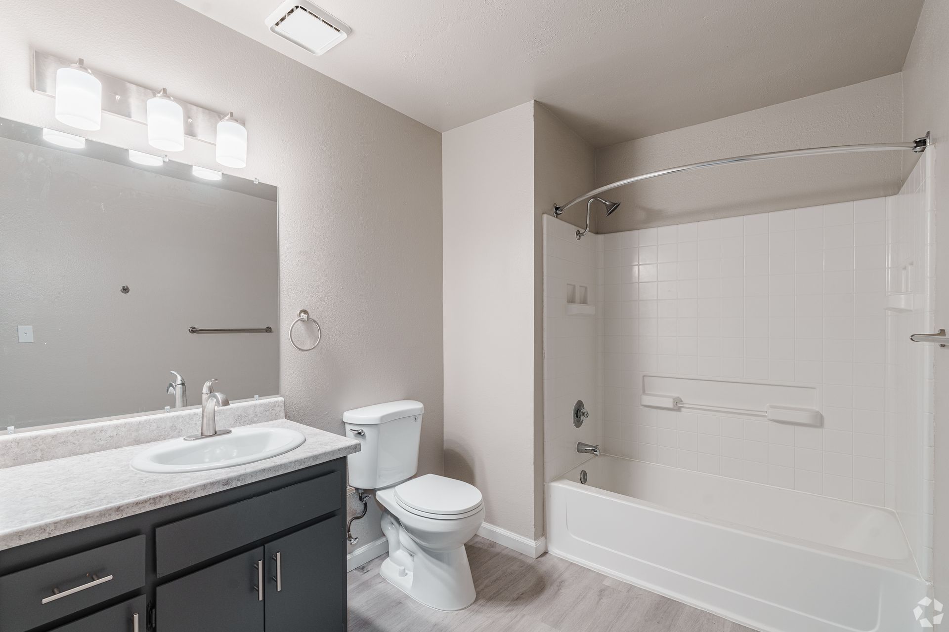 Bathroom with a white tub/shower, toilet, vanity, and gray walls; light gray floor.
