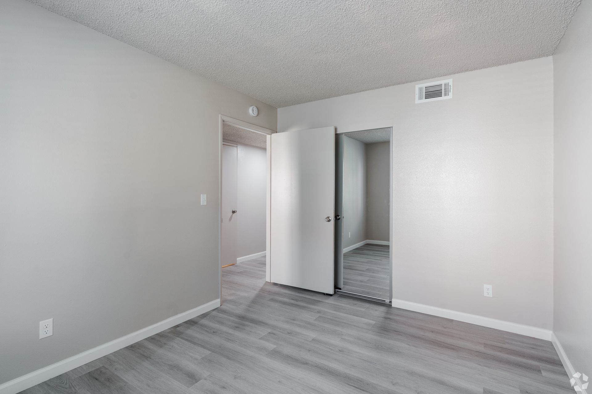 Empty bedroom with gray walls, light wood flooring, and a closet with folding doors.