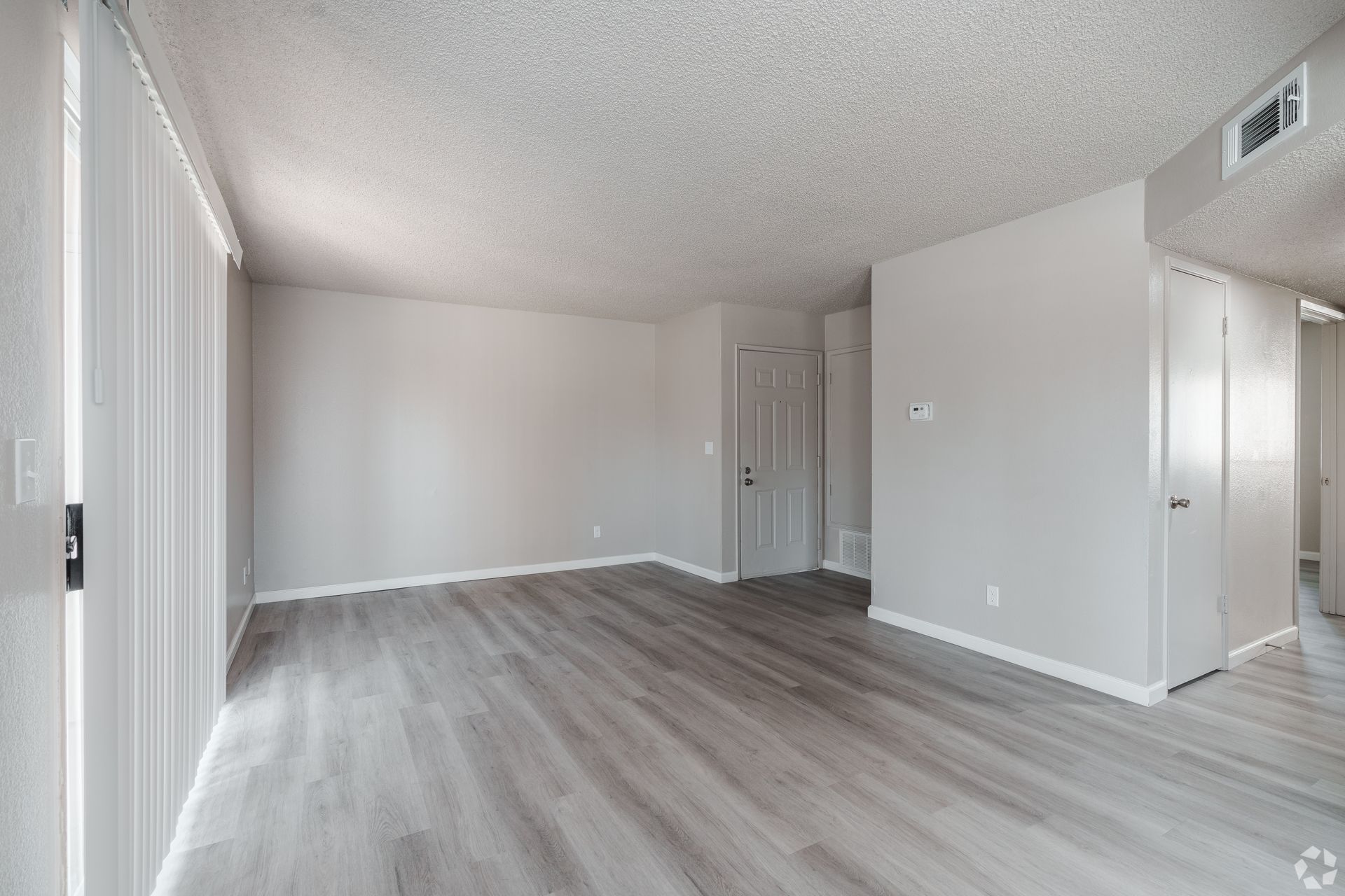 Empty apartment room with gray walls and flooring, sliding door, and white door.