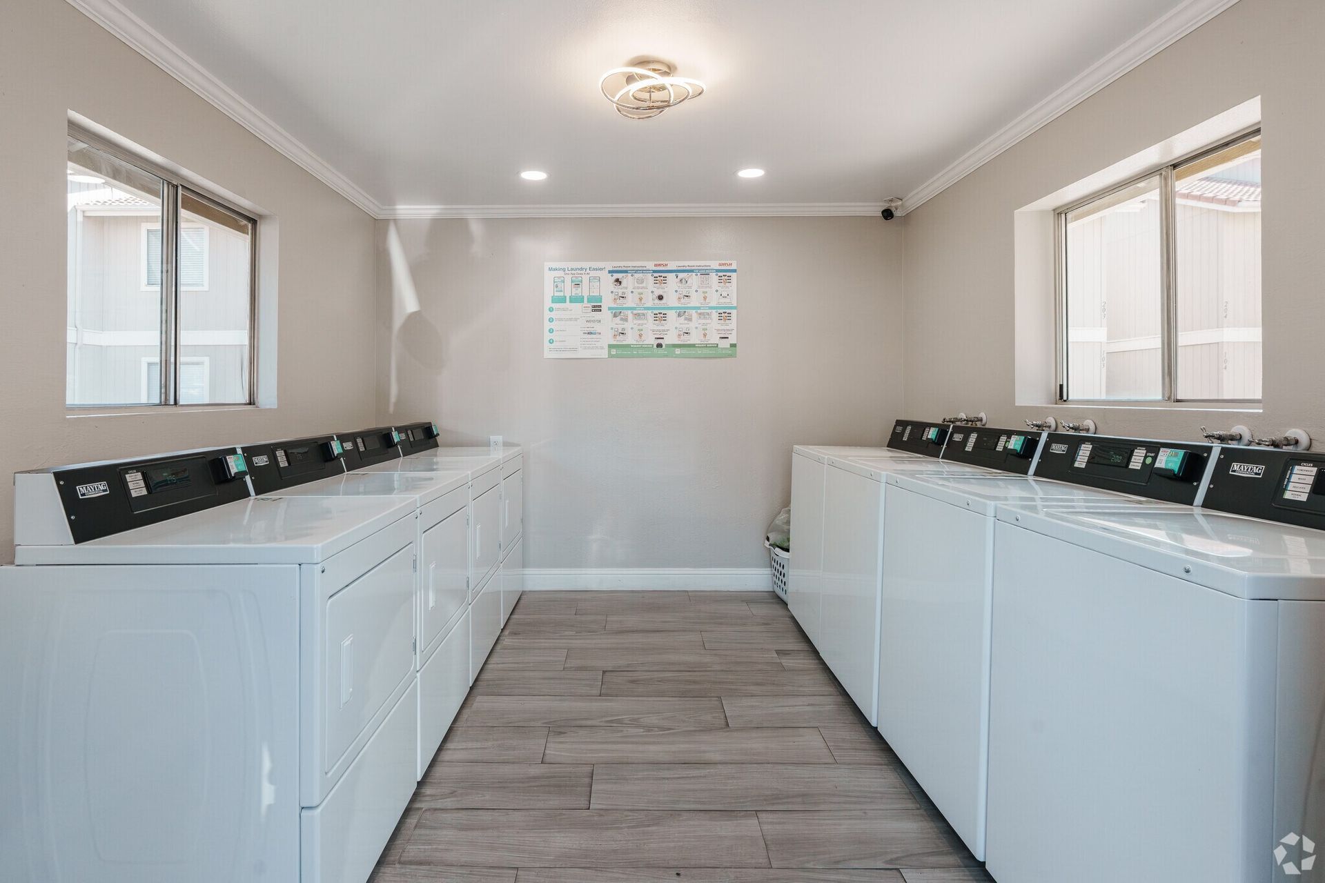Laundry room with white washers and dryers, wood floor, window, bulletin board.