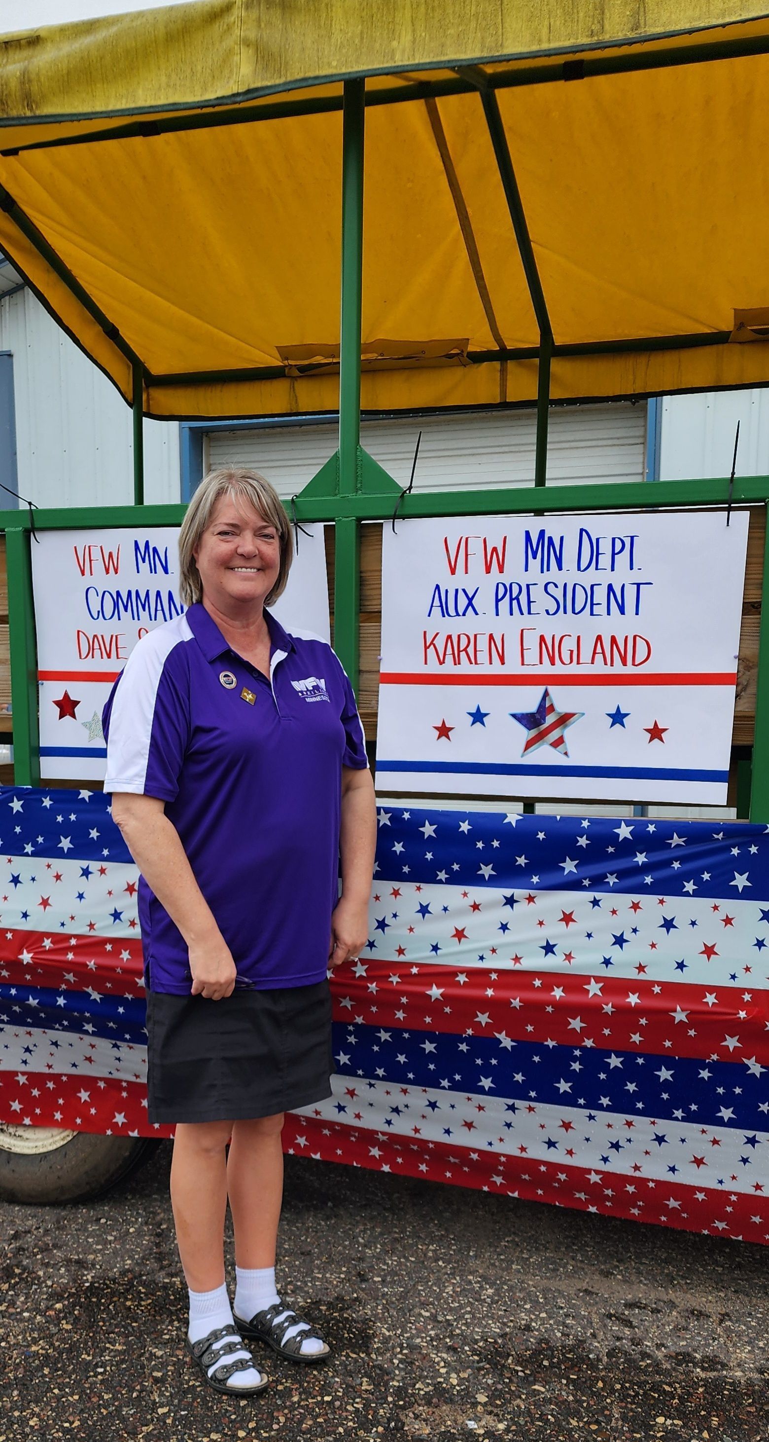 Woman in purple shirt stands in front of a patriotic float.