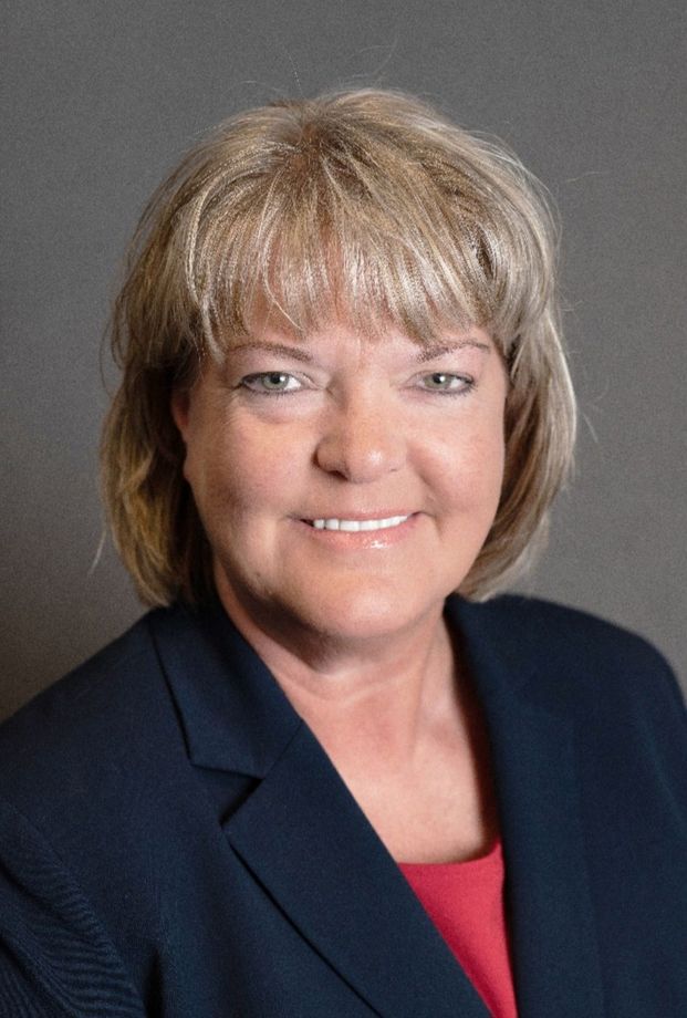 Woman with short, blonde hair smiles, wearing a navy blazer over a red top.