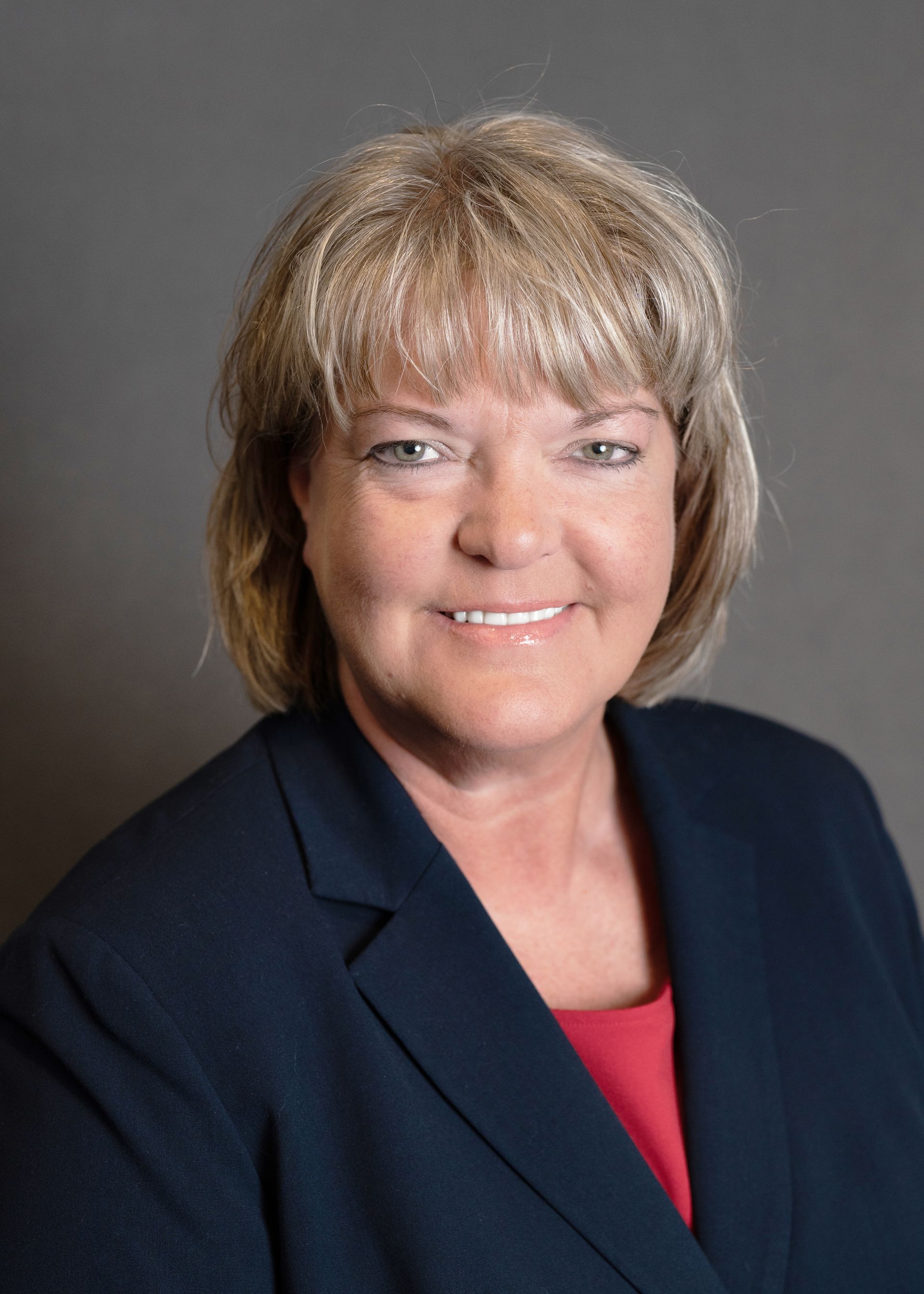 Woman in a navy blazer and red top smiles against a gray background.