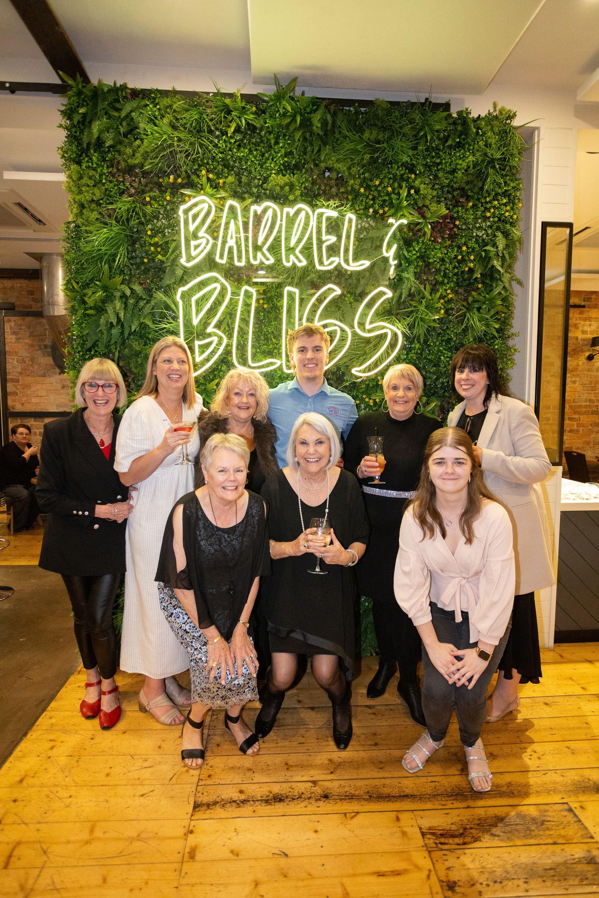 Group of people posing in front of a green wall with neon sign 