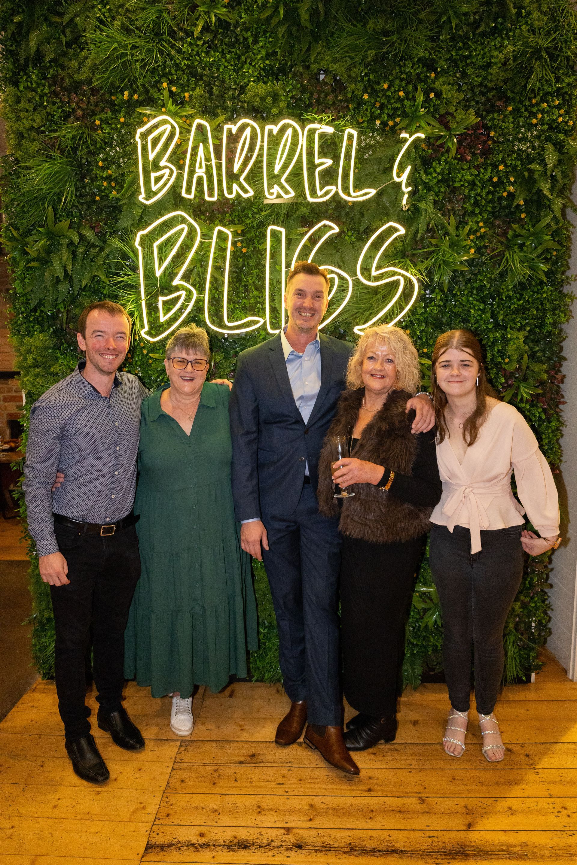Five people posing in front of a neon sign that reads 