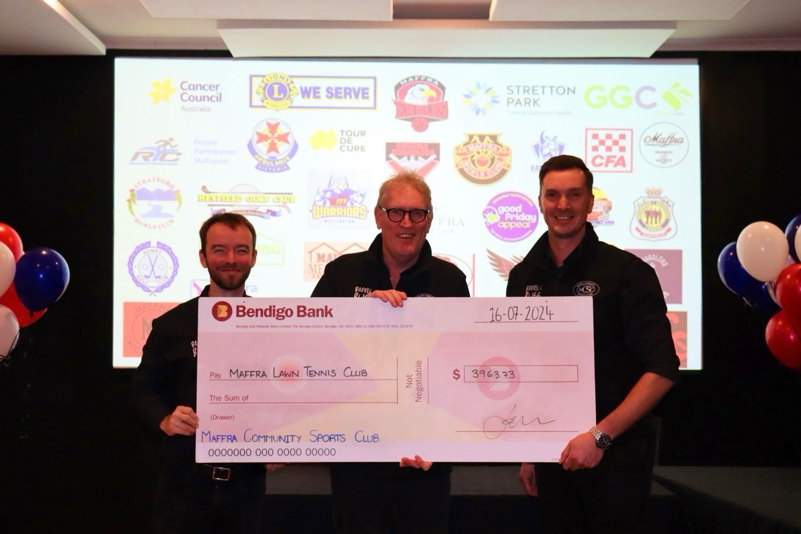 Three men hold a giant check from Bendigo Bank. They stand in front of a logo-filled screen.