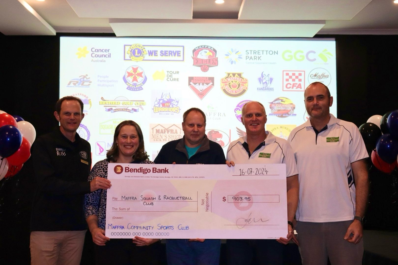 Five people holding a large check, sponsored logos in the background.
