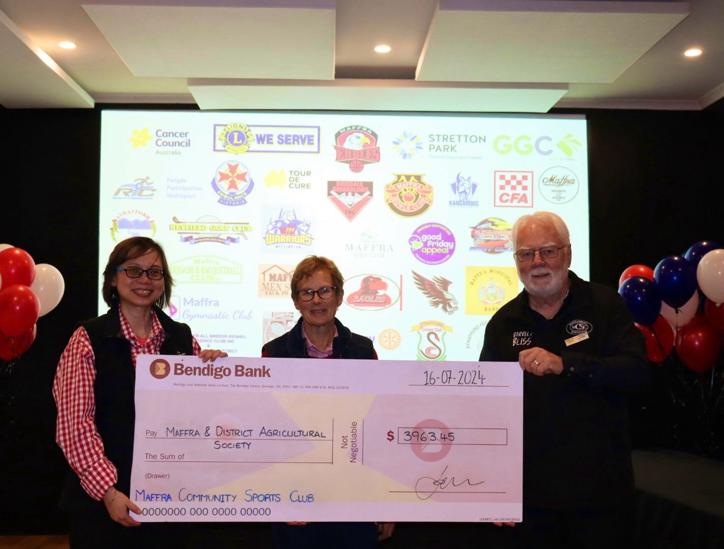 Three people holding a large check from Hondaje Bank at a Marine Community Grants event.