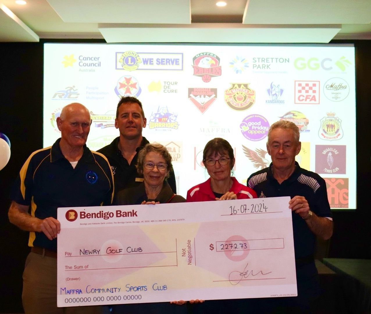 Group of people holding a large check from Bendigo Bank. Sponsors' logos are displayed behind them.