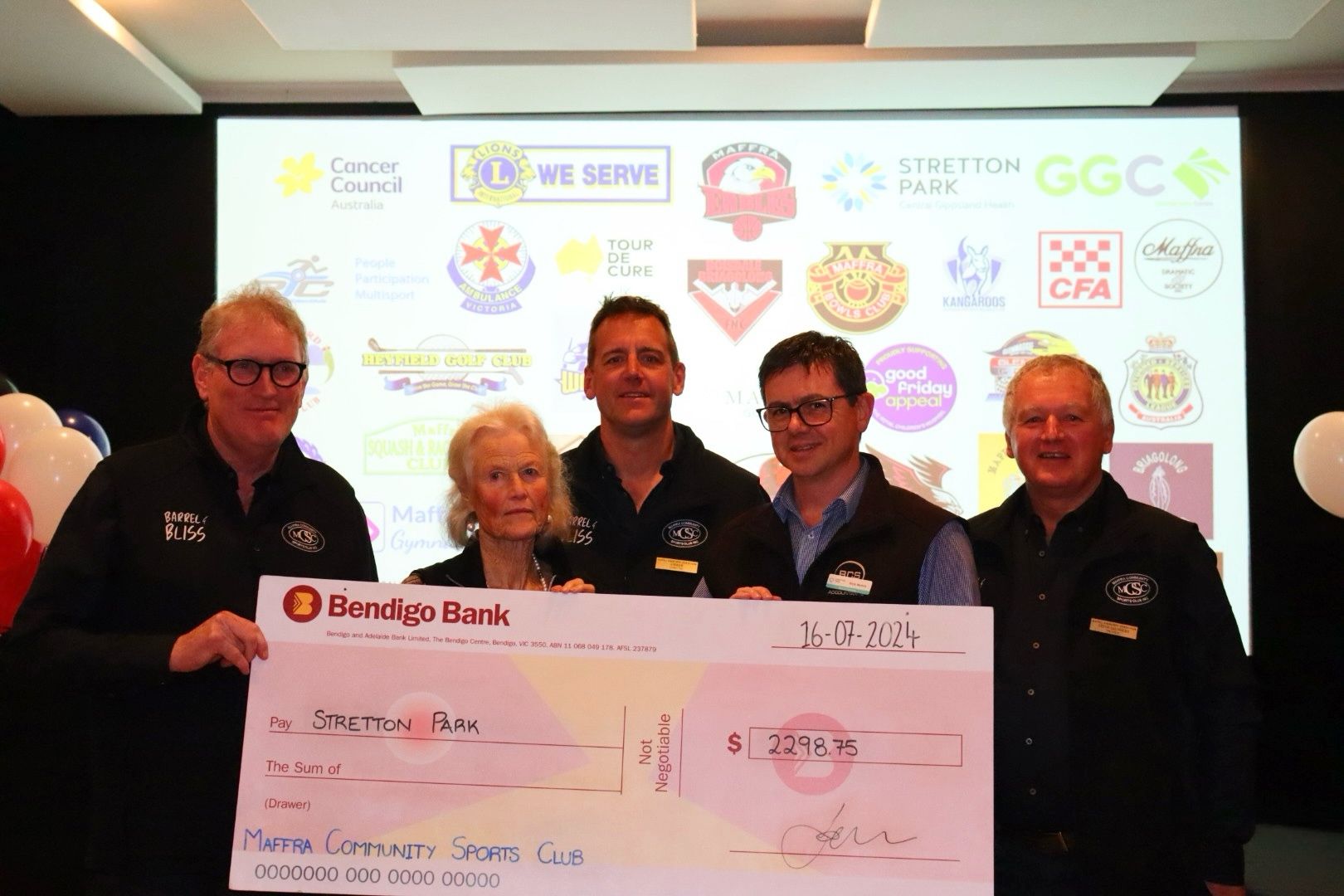Group holding large check for charity in front of a wall with logos.
