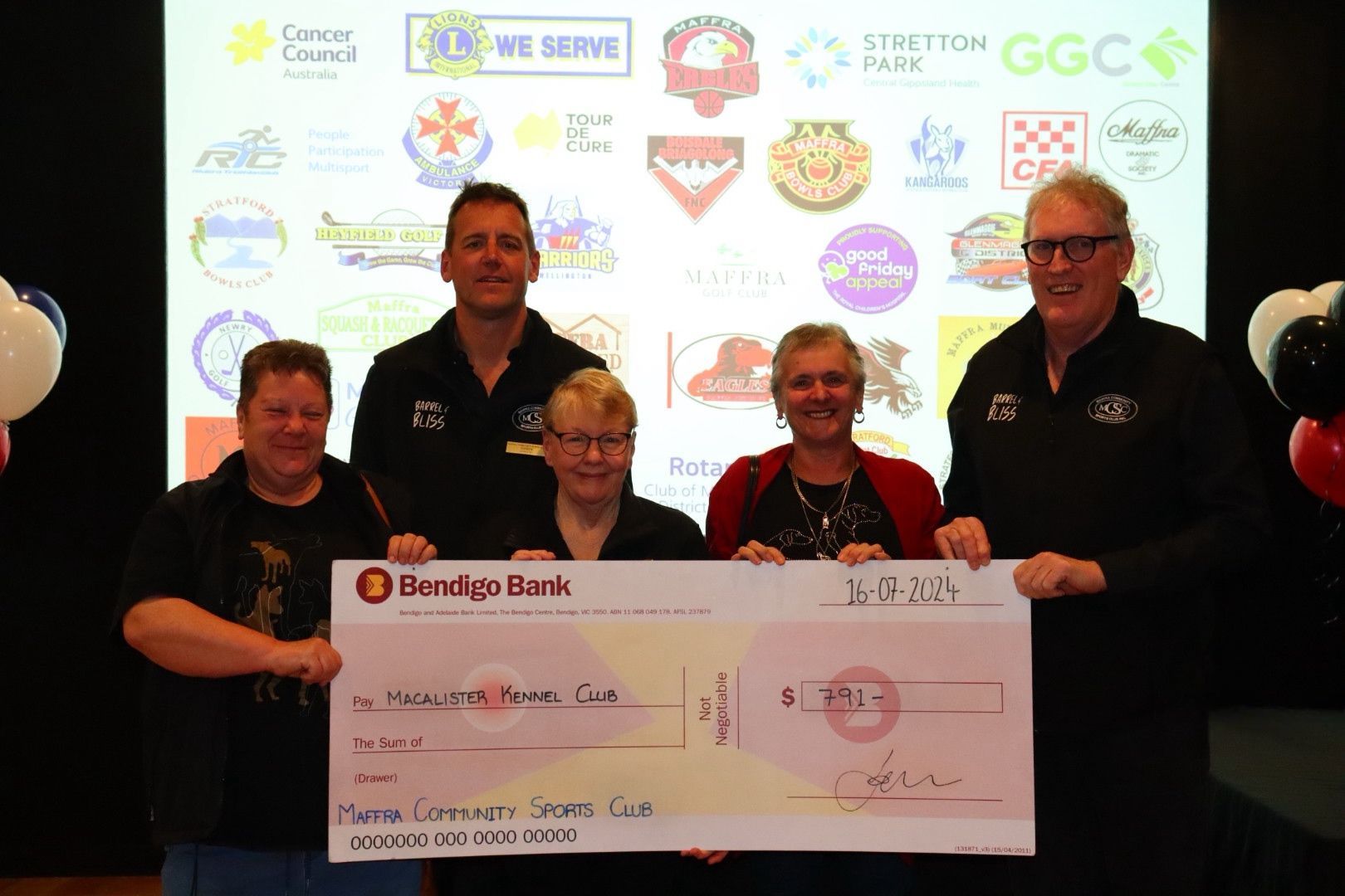 People holding a large check in front of a backdrop with logos, indoors.