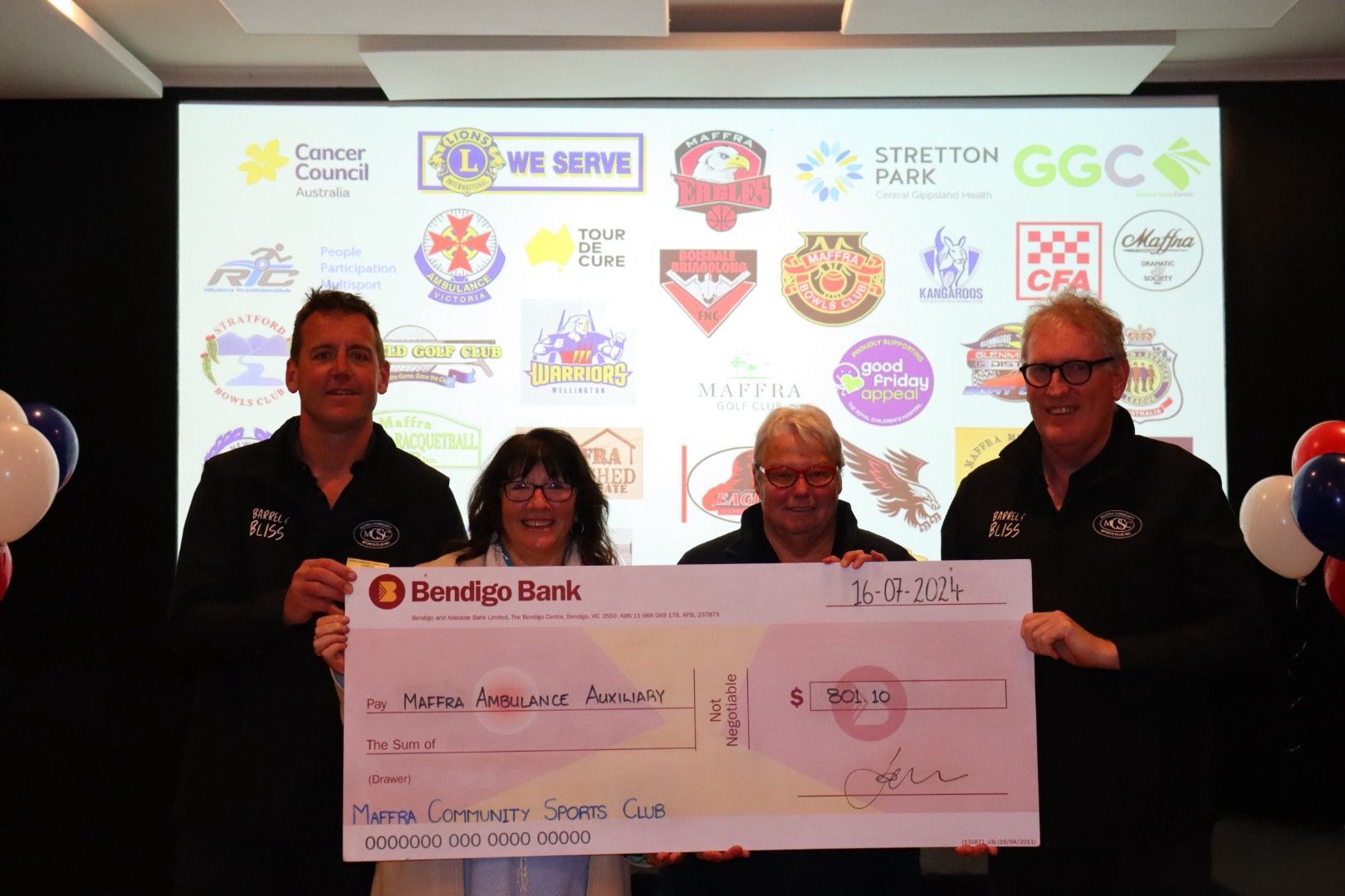 Four people holding a large check in front of a backdrop with logos. They are smiling.