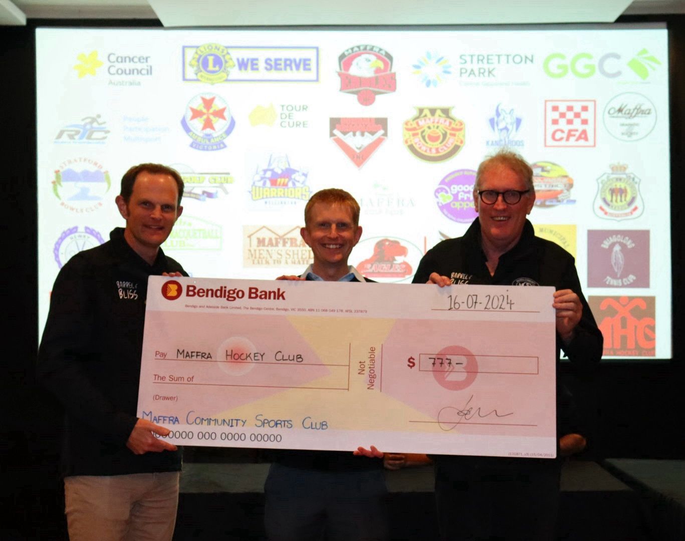 Men holding a large check for $295 in front of a projector screen with logos.