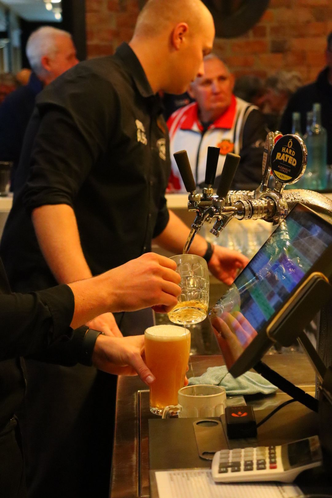 Bartender pouring beer, interacting with a customer at the bar; other patrons in the background.