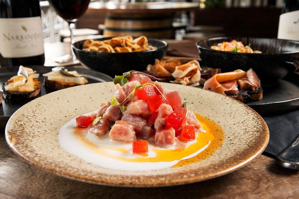 Close-up of tuna tartare with other dishes on a table, wine and barrell background.