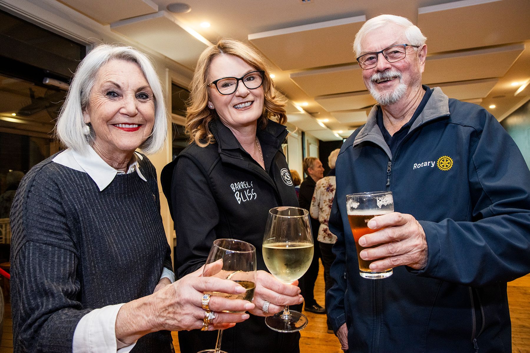 Three people toasting with drinks at an event; woman on the left smiles, others look at the camera.