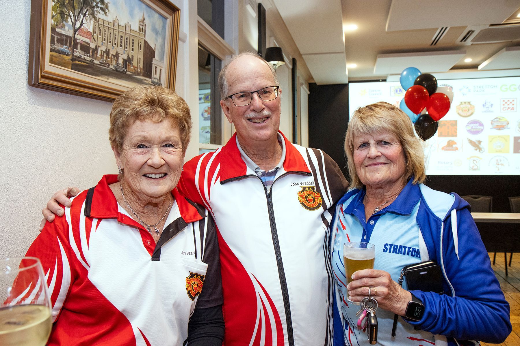 Three smiling people in sports attire pose together indoors.