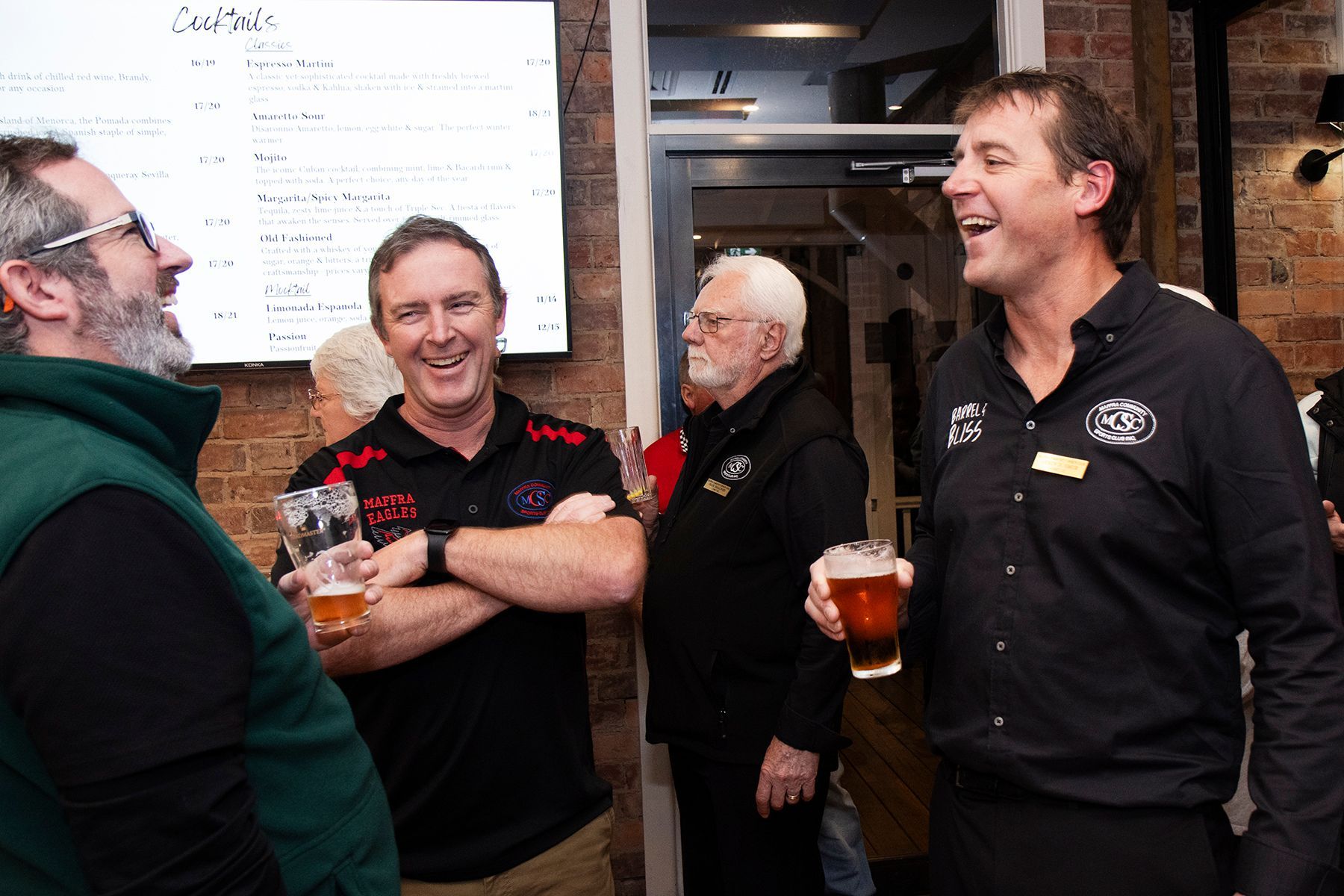 Men laughing and drinking beer in a pub, by a menu.