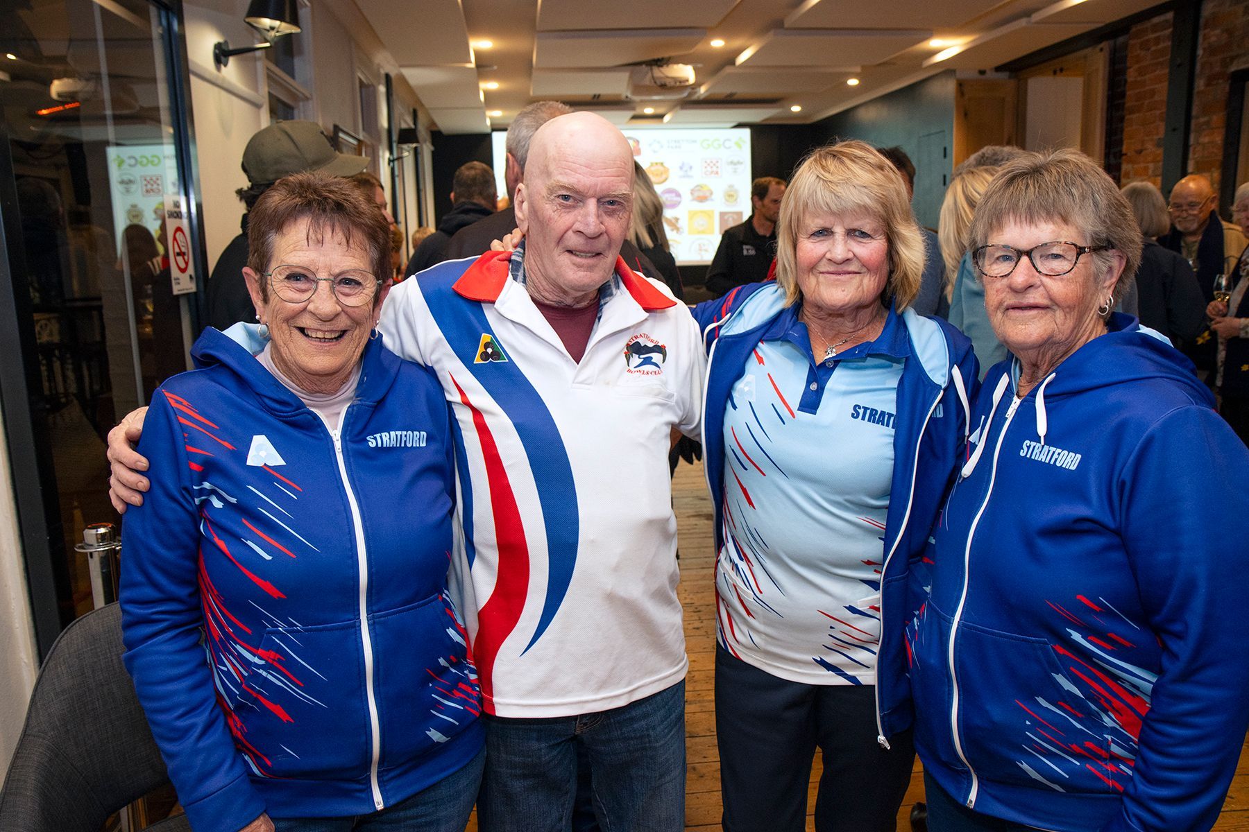Four people in sports attire pose together indoors; two women embrace.