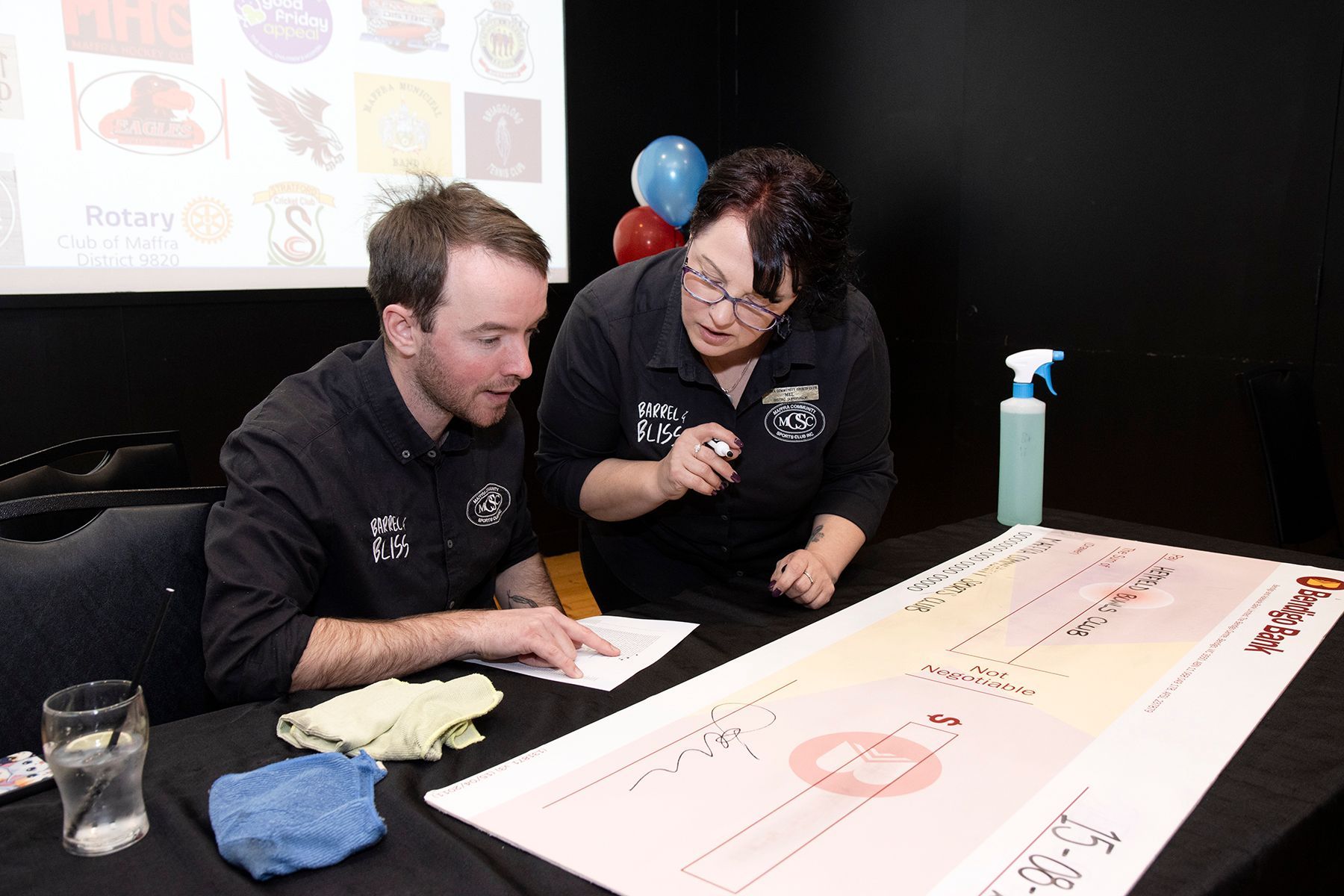 Two people at a table, looking at a paper with a diagram. One is pointing while the other looks on.