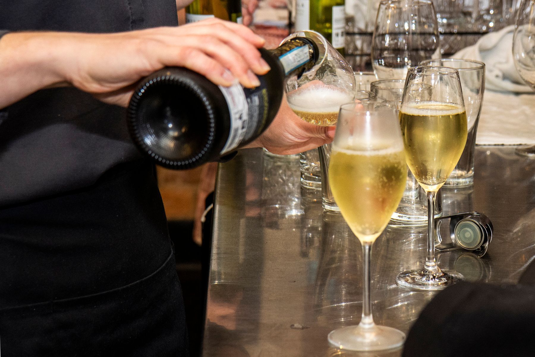 Person pouring champagne into fluted glasses at a bar.