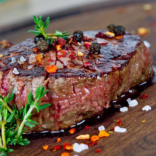 Grilled steak seasoned with herbs, salt, pepper, and red pepper flakes on a wooden surface.
