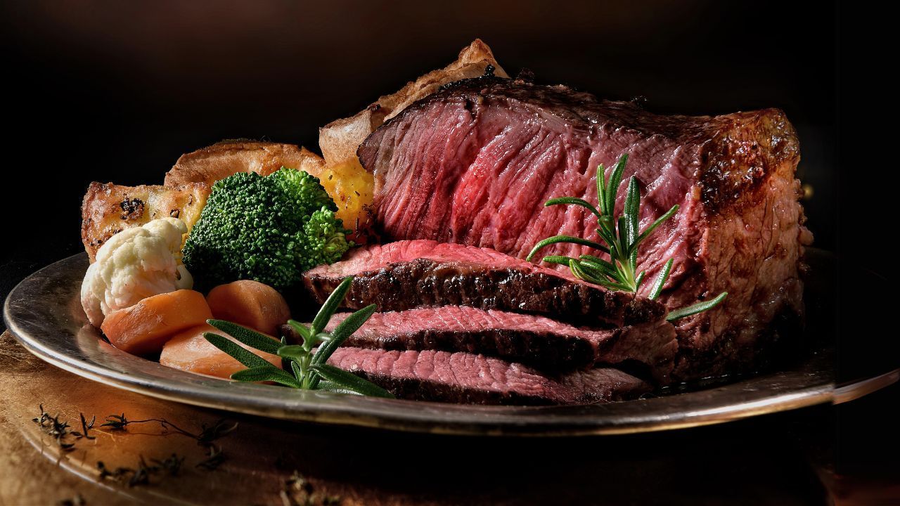 A plate of roasted prime rib, sliced, with vegetables and herbs.
