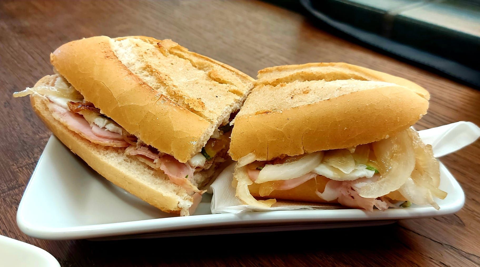 Sándwich cortado por la mitad en un plato blanco; lleva relleno de jamón y cebolla.