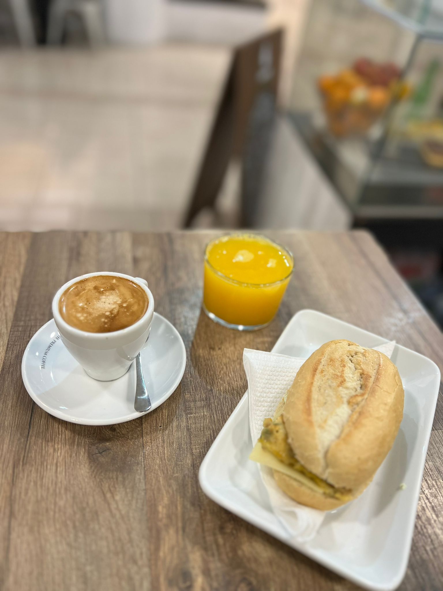 Capuchino, zumo de naranja y sándwich en una mesa de madera de un café.