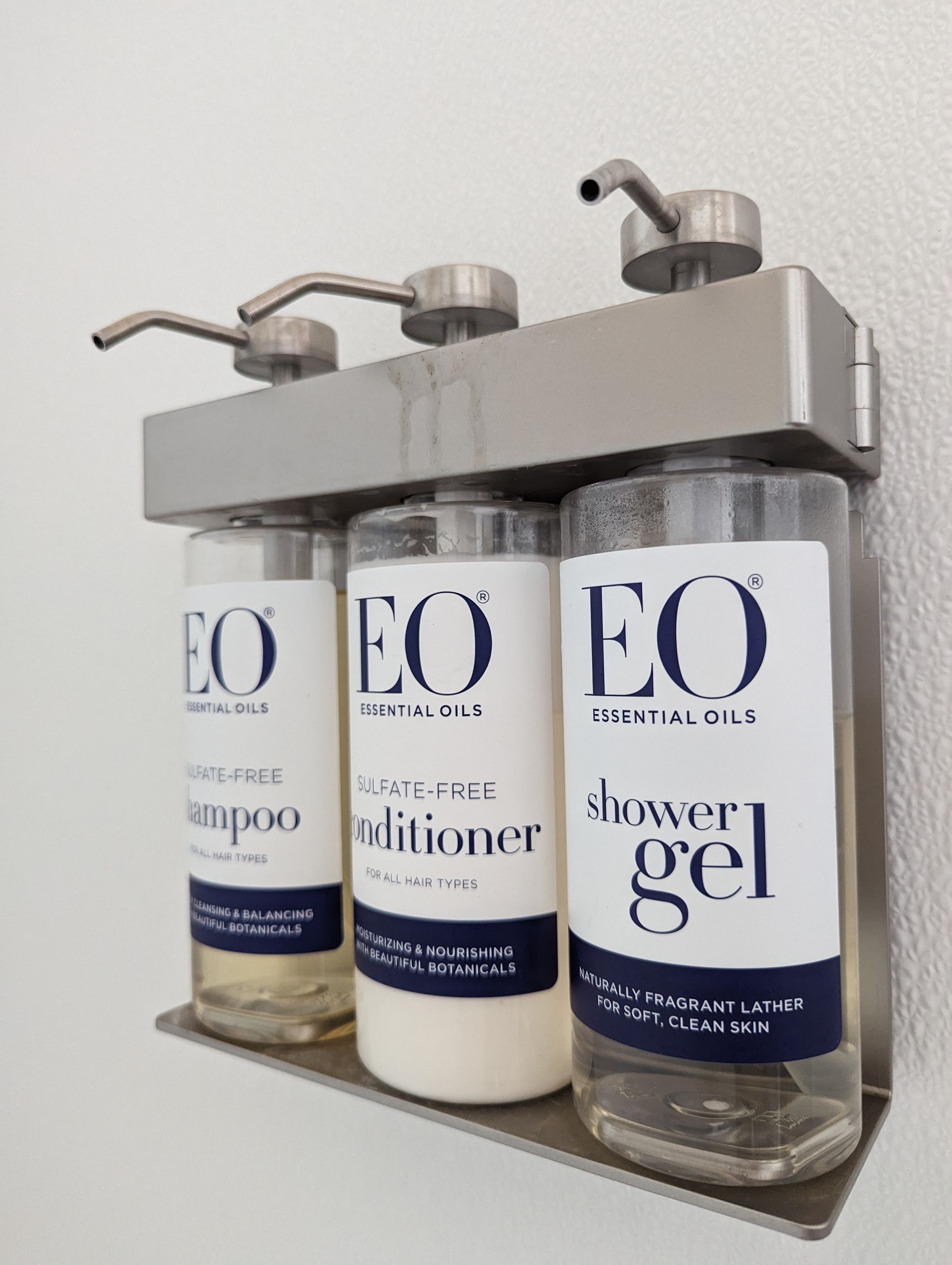 Three bottles of eo shampoo conditioner and shower gel are hanging on a wall
