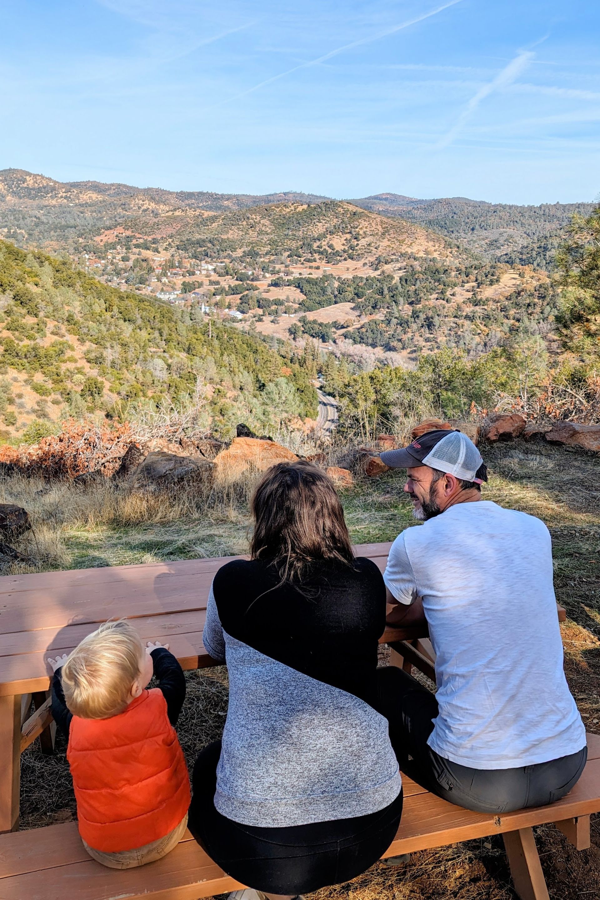 A family is sitting on a picnic table looking at the mountains.