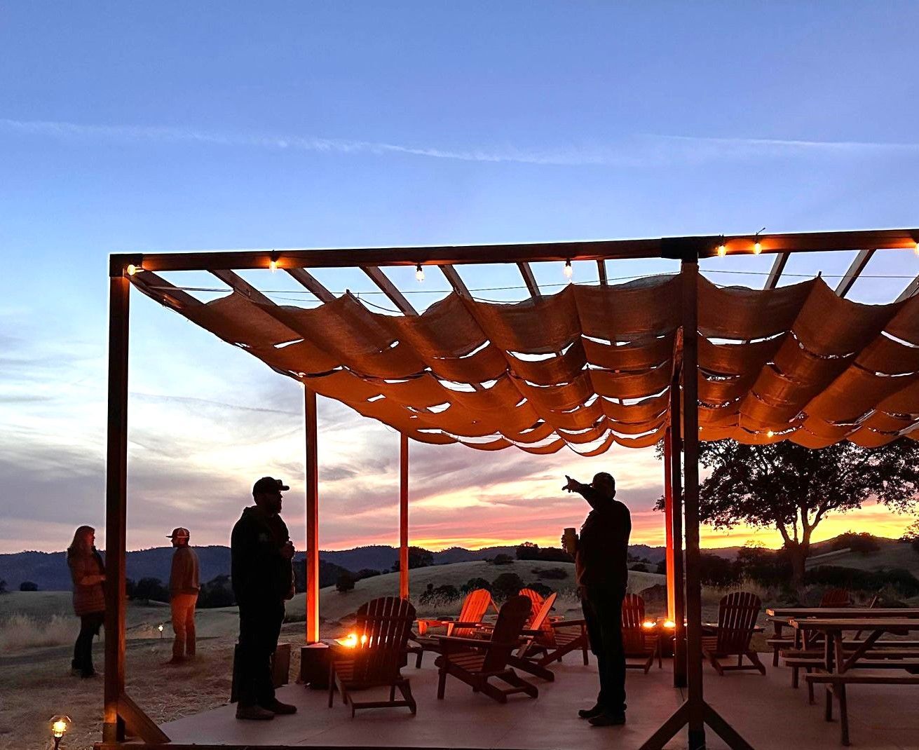A group of people standing under a canopy at sunset