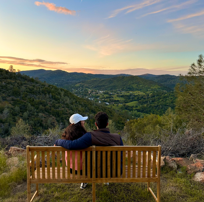 A man and a woman are sitting on a bench overlooking a valley.