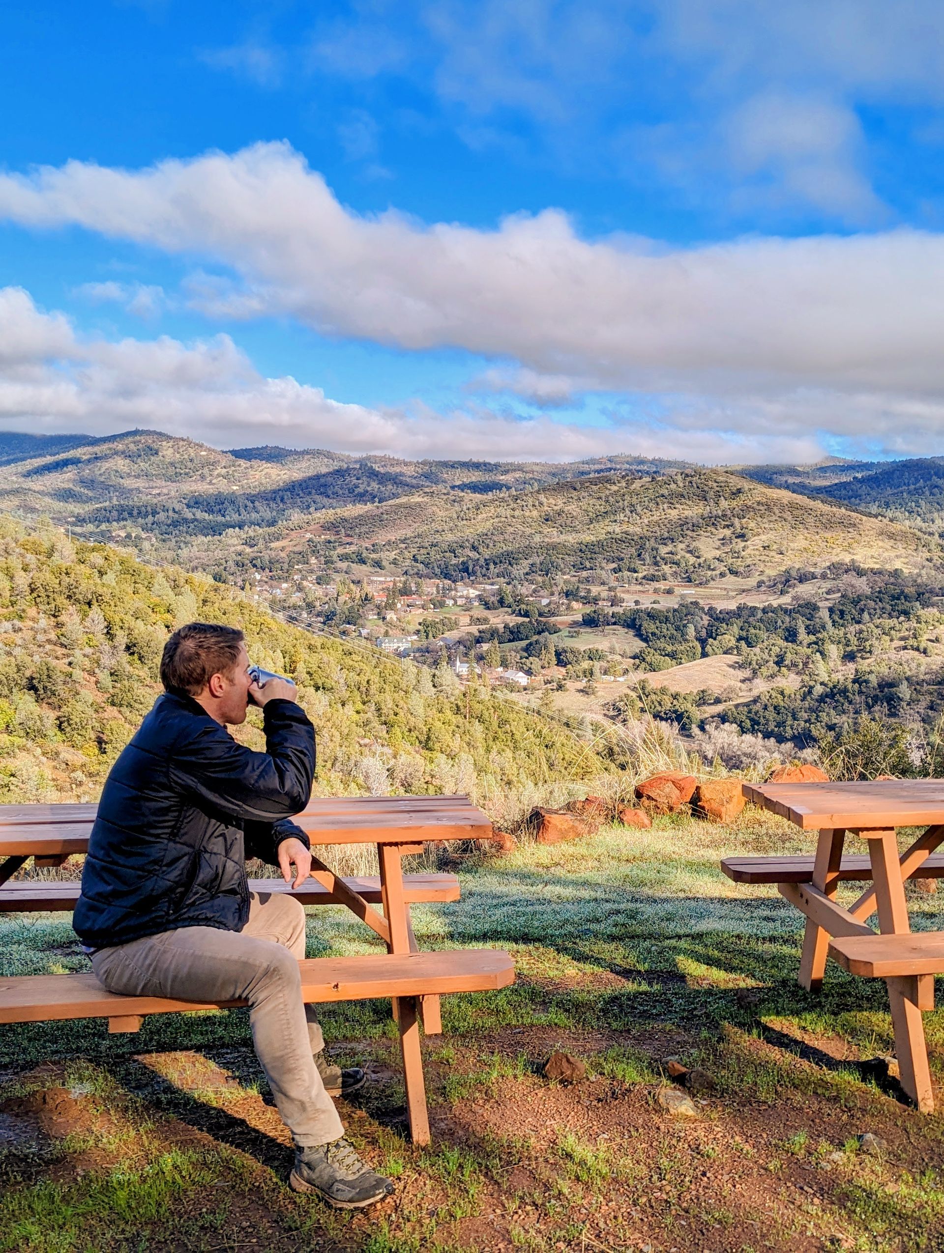 A man is sitting at a picnic table overlooking a valley.