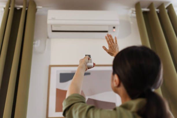 A woman is adjusting the air conditioner with a remote control.