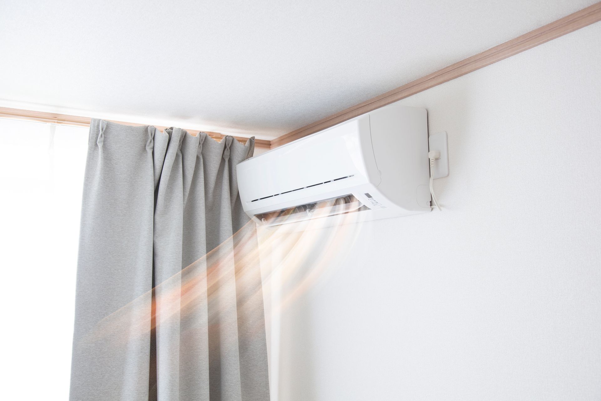 A white air conditioner is hanging on a white wall next to a window.