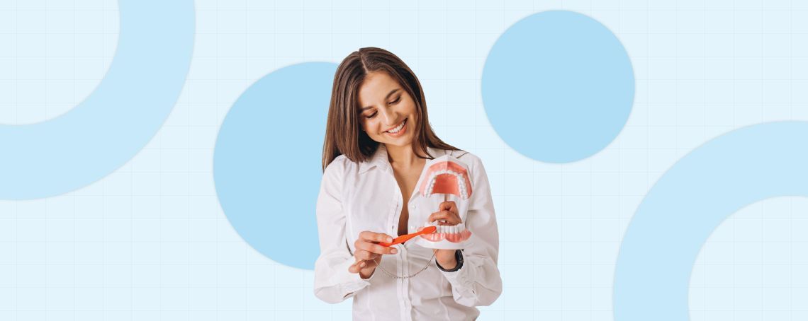 A smiling woman in a white coat holds a model, pointing, against a light blue background.
