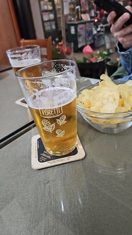 Due pinte di birra, patatine e una persona che tiene in mano un telefono su un tavolo in un bar.