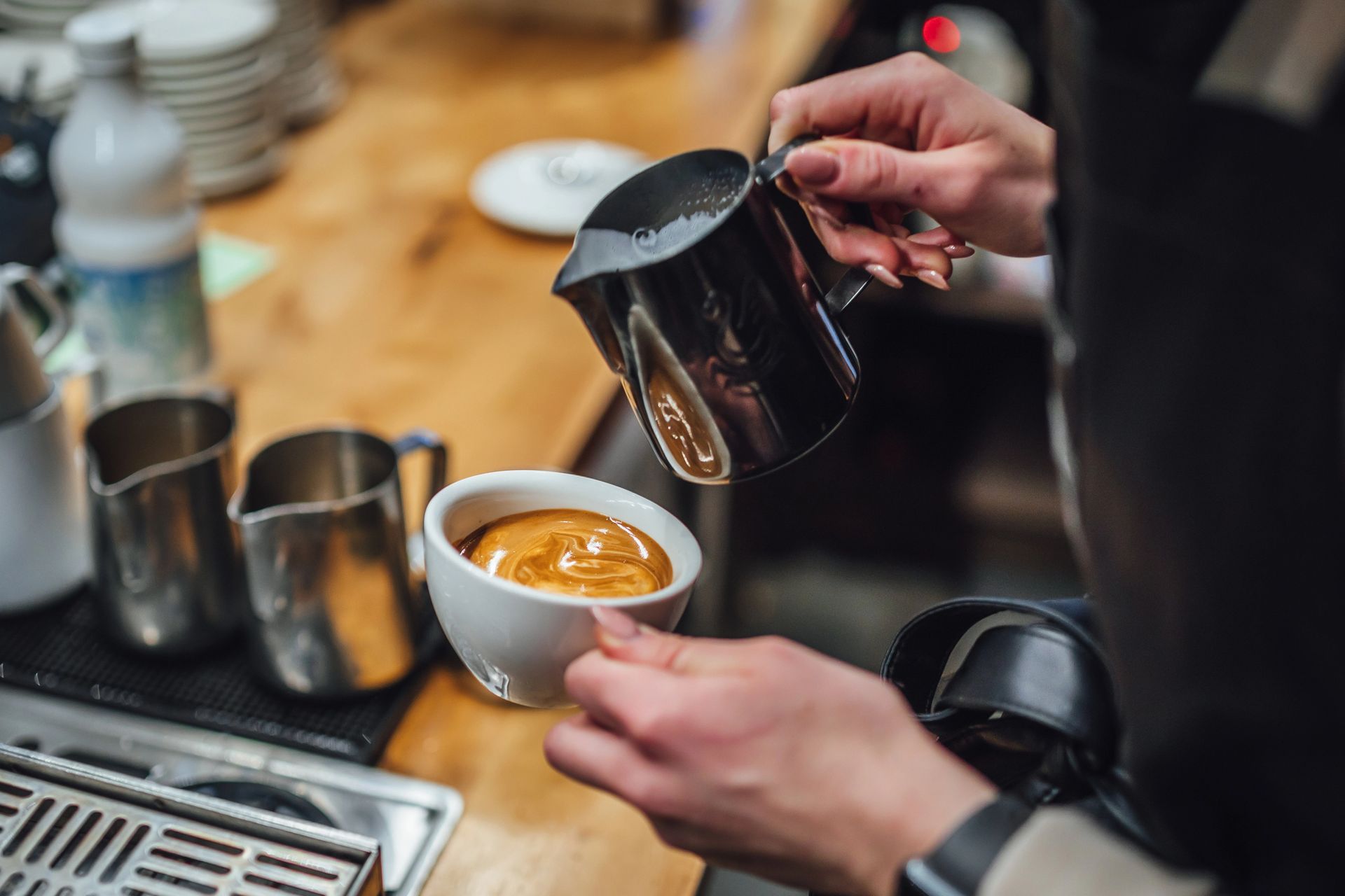 Barista che versa il latte da una brocca di metallo in una tazza di caffè.