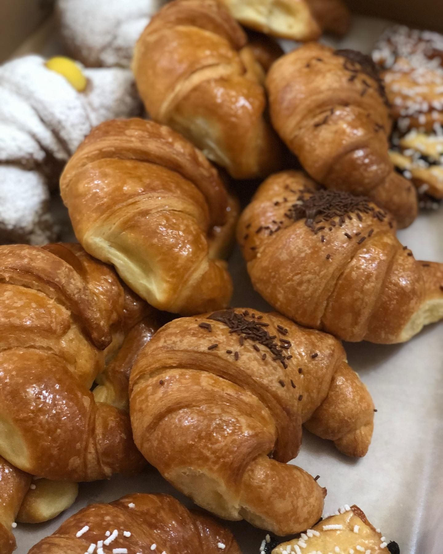 Una pila di croissant dorati con glassa lucida e granella di cioccolato, accanto ad altri pasticcini.