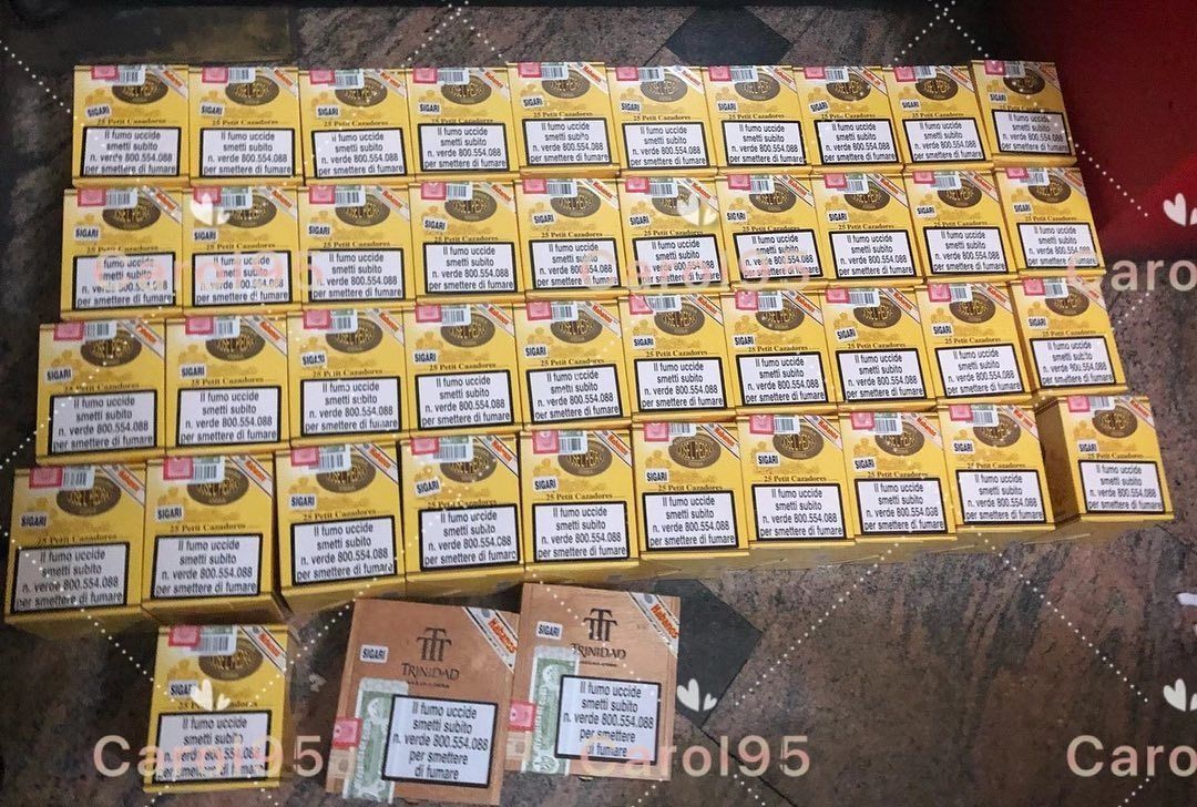 Scatole di sigarette gialle e marroni, disposte in molte file su una superficie scura.