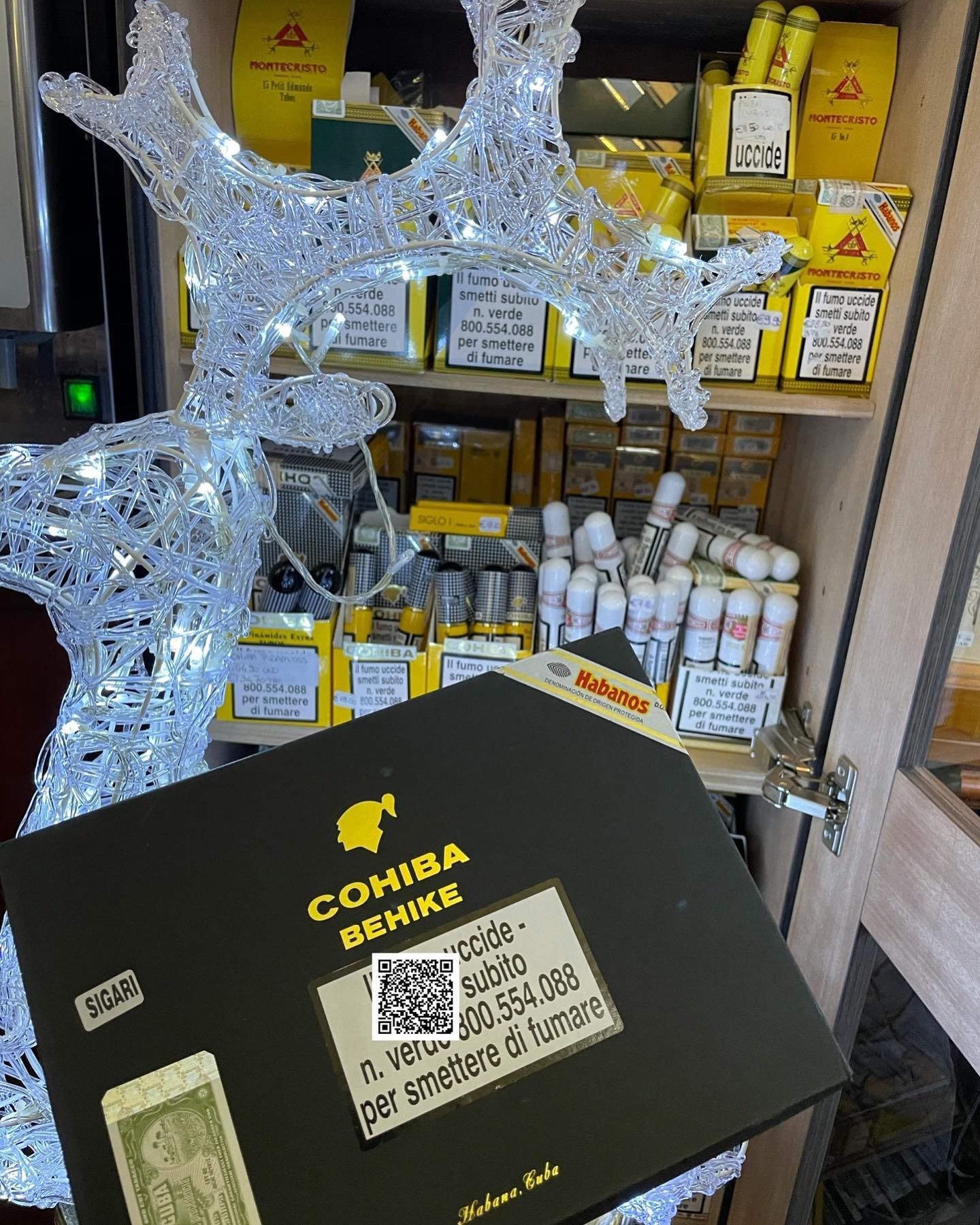 Uno scaffale pieno di sigari; in primo piano c'è una scatola di sigari Cohiba Behike, con una renna decorativa accesa.