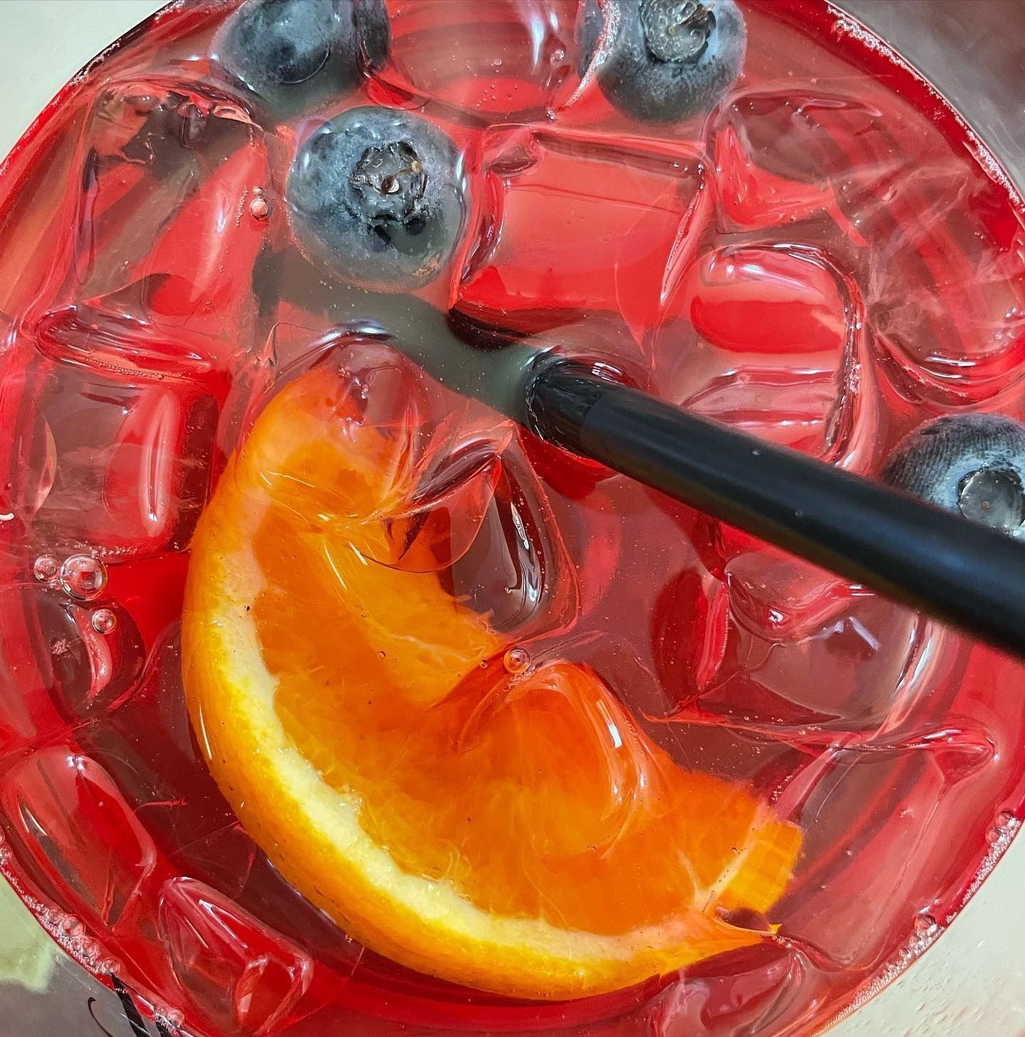 Bevanda rossa con ghiaccio, mirtilli e fetta d'arancia, con cannuccia nera in un bicchiere.