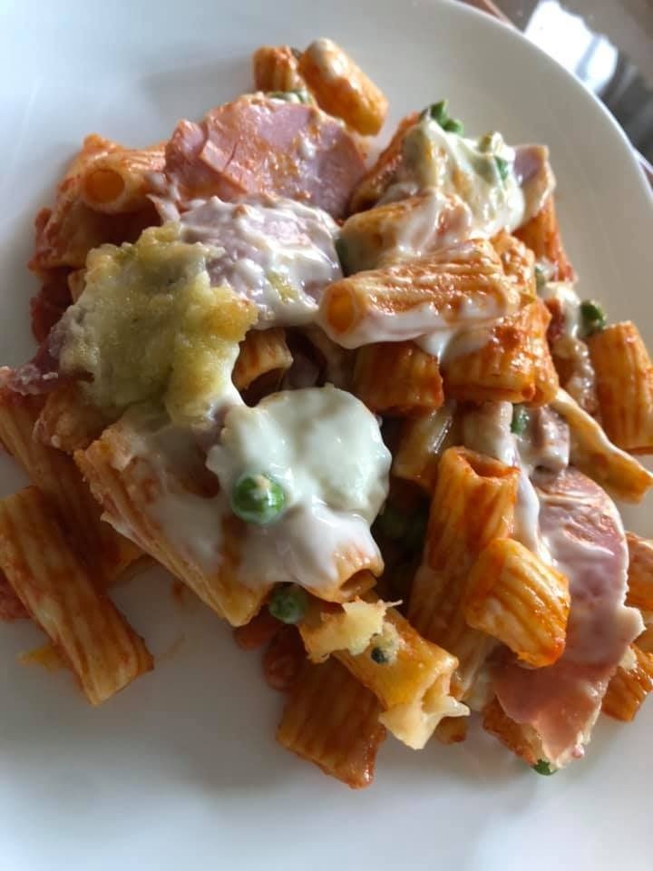 Piatto di pasta con rigatoni, salsa di pomodoro, piselli, prosciutto e besciamella.